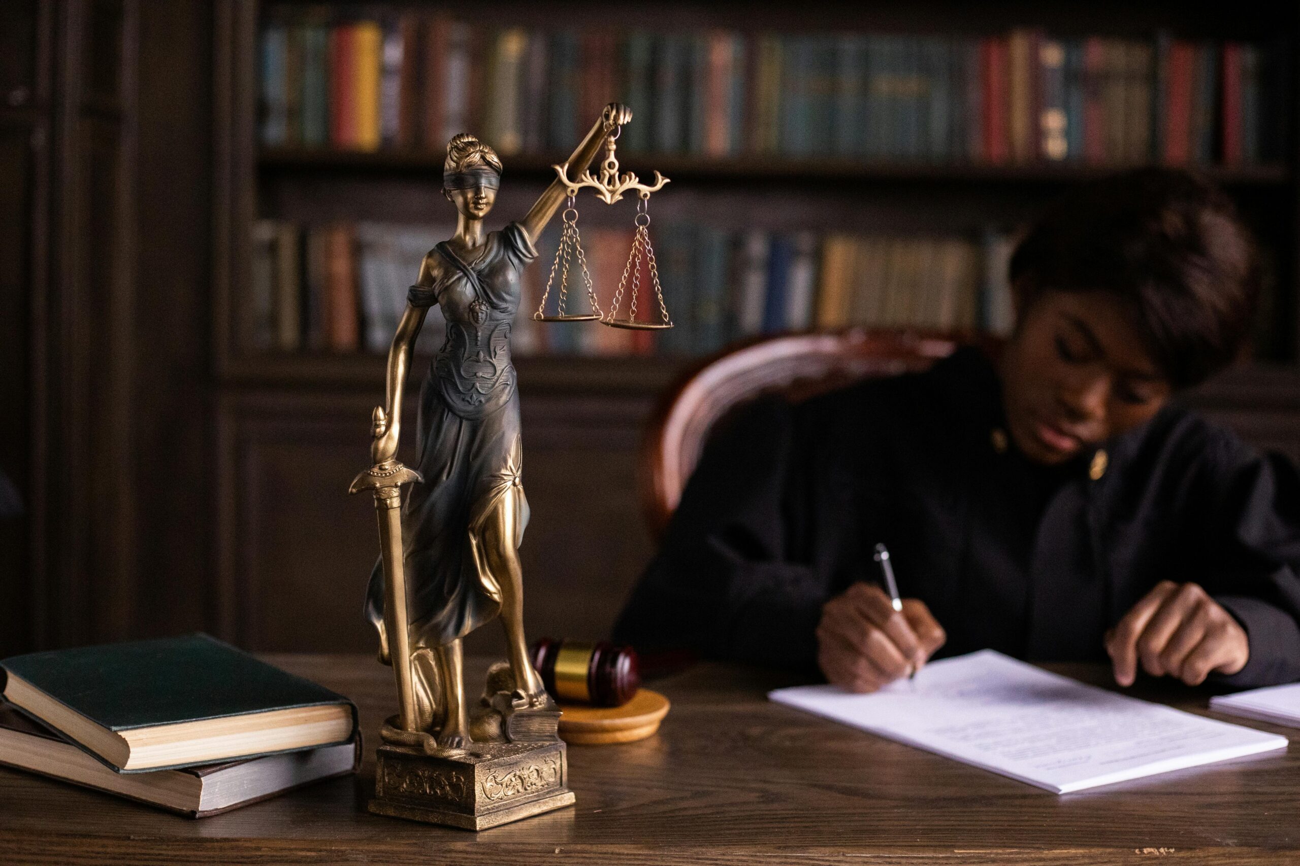 Femme africaine en tenue sombre rédigeant à son bureau, entourée d'ouvrages juridiques