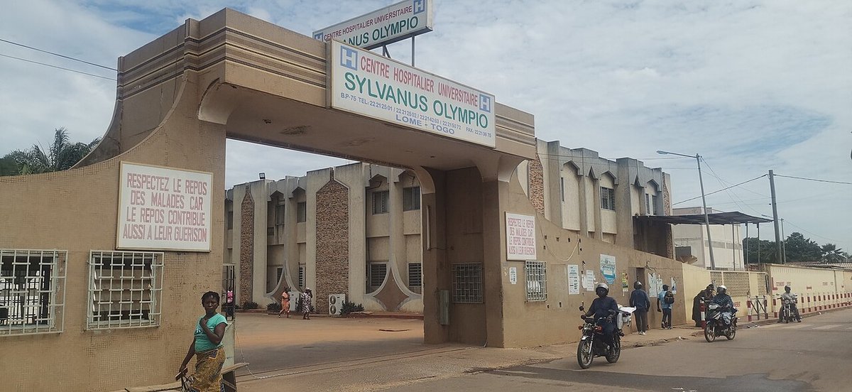 Entrée du Centre hospitalier universitaire Sylvanus Olympio à Lomé, des conducteurs de moto-taxi passant devant