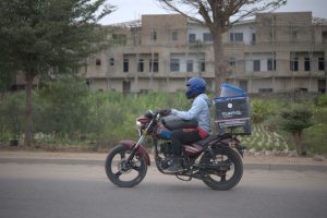 salarié déguisé - livreur à moto avec caisson de livraison dans une rue d’Afrique de l’Ouest