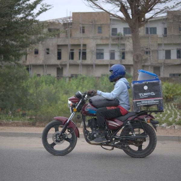 salarié déguisé - livreur à moto avec caisson de livraison dans une rue d’Afrique de l’Ouest
