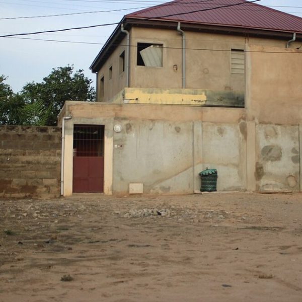 Acheter un terrain au Togo : parcelle en terre battue devant une maison inachevée et un mur de parpaings à Lomé