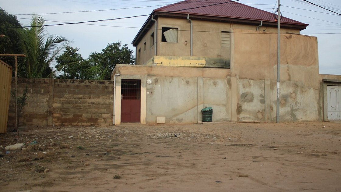 Acheter un terrain au Togo : parcelle en terre battue devant une maison inachevée et un mur de parpaings à Lomé