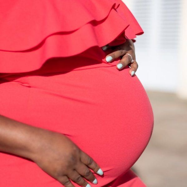 Congé de maternité au Togo : femme enceinte en robe rouge, les mains posées sur son ventre