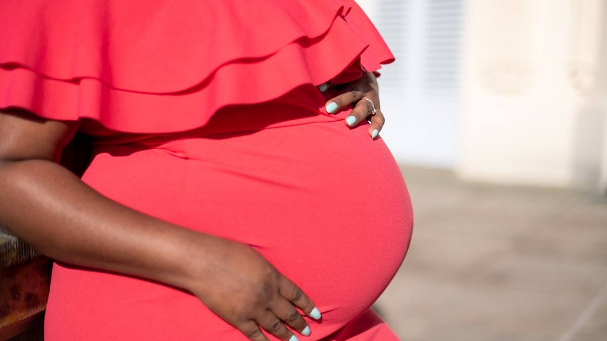 Congé de maternité au Togo : femme enceinte en robe rouge, les mains posées sur son ventre