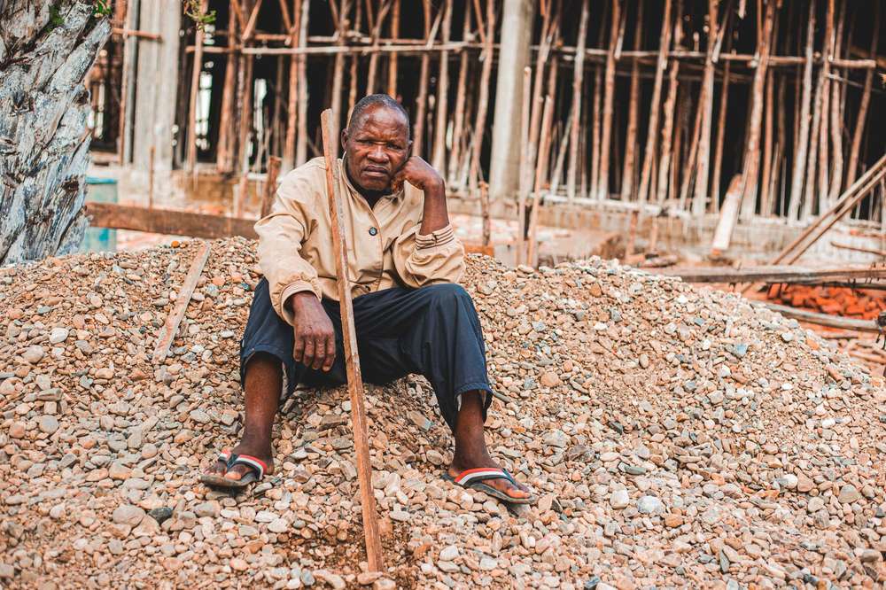 Retraite au Togo : un ouvrier âgé assis sur un tas de gravier devant un chantier en construction